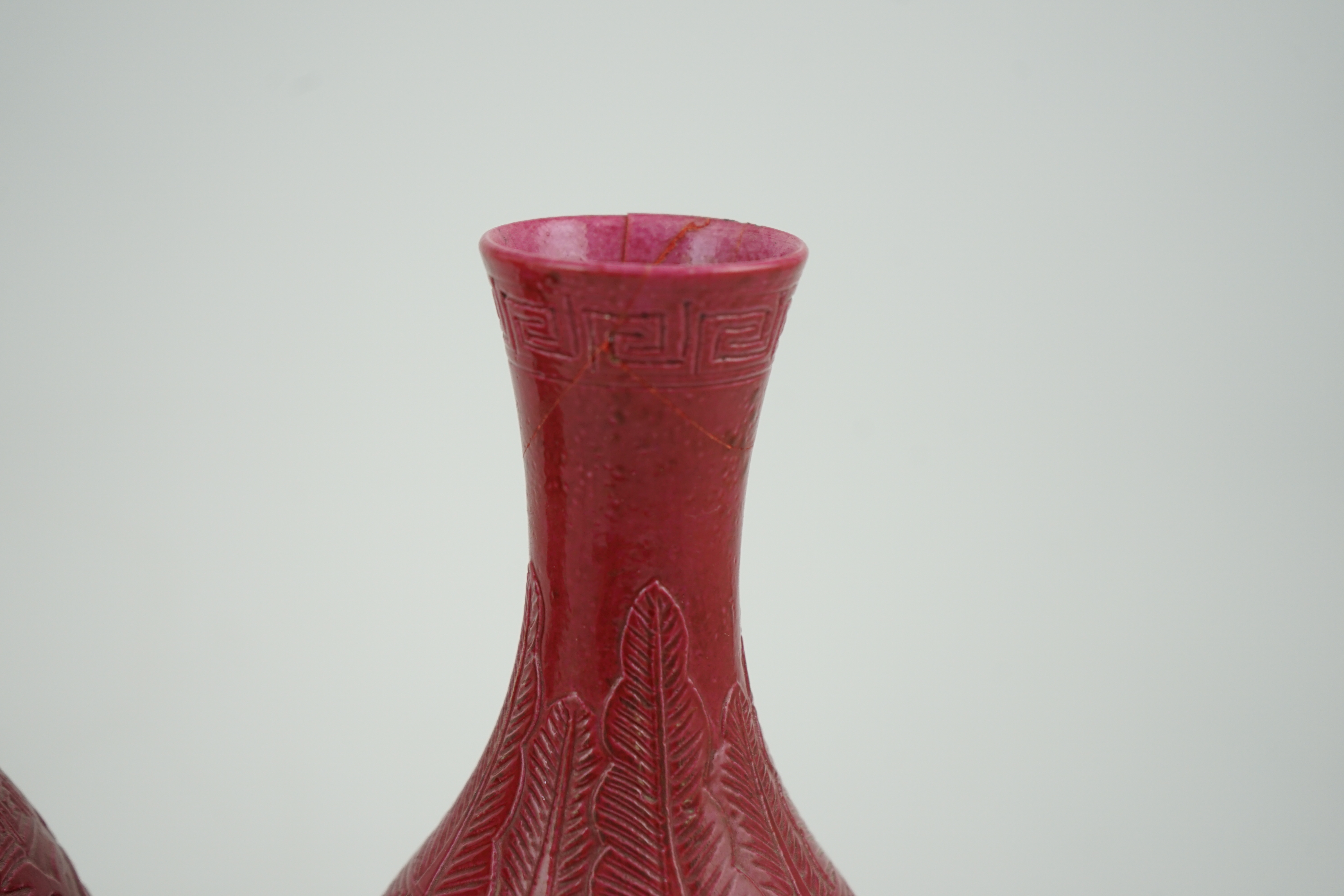 A pair of Chinese ruby ground ‘lotus’ bottle vases, late 19th century, each carved in relief with lotus flowers, scrolling tendrils and leaves, both with carved stands, 24cm high. Condition - one vase the neck broken bot